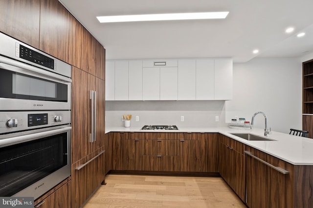 kitchen with sink, appliances with stainless steel finishes, kitchen peninsula, light hardwood / wood-style floors, and white cabinets