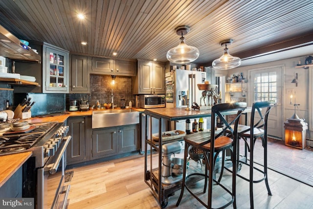 kitchen with sink, wooden counters, hanging light fixtures, premium appliances, and light hardwood / wood-style floors