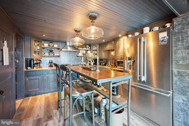 kitchen with wall chimney range hood, light hardwood / wood-style flooring, appliances with stainless steel finishes, hanging light fixtures, and wood counters