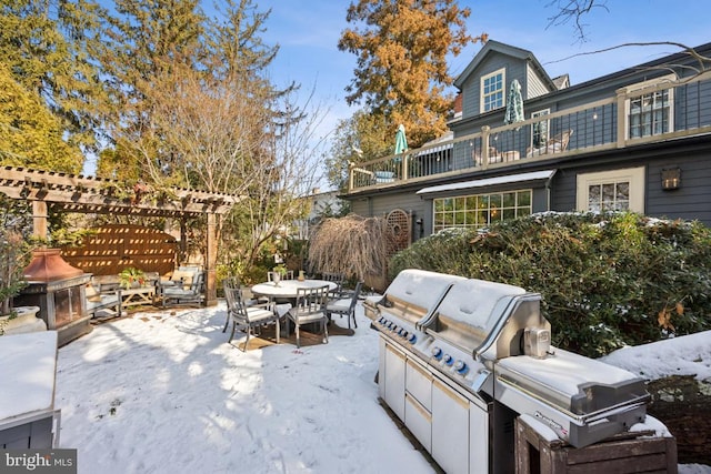 snow covered patio featuring a pergola, a balcony, and exterior kitchen