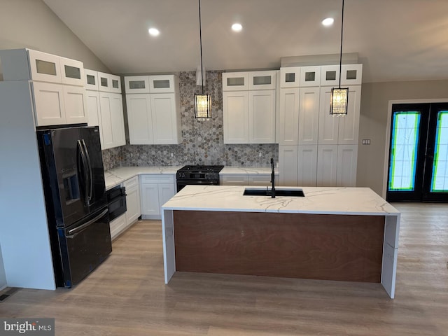 kitchen with decorative light fixtures, light stone countertops, a kitchen island with sink, and black appliances