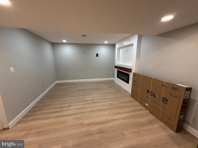 basement featuring a large fireplace and light hardwood / wood-style floors