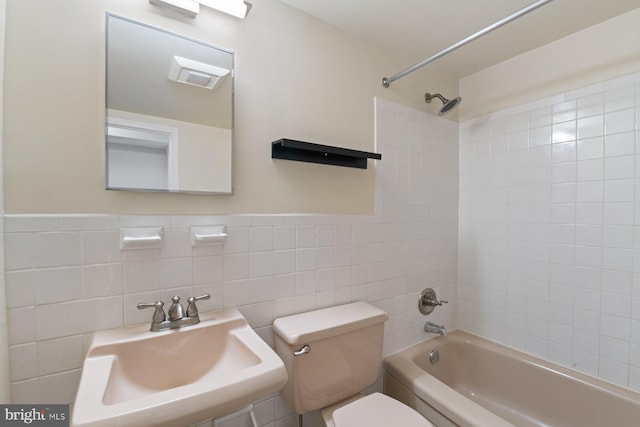 full bathroom featuring toilet, tiled shower / bath combo, sink, and tile walls