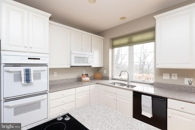 kitchen featuring black appliances, light stone counters, a sink, and white cabinetry