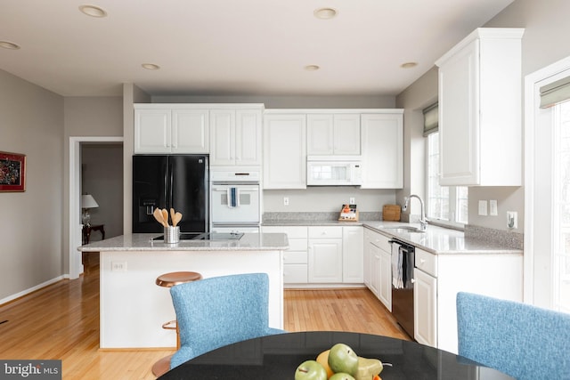 kitchen featuring white cabinetry, a sink, light wood finished floors, and black appliances