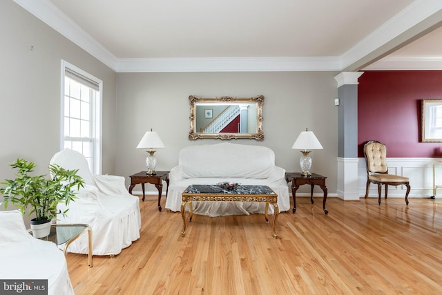 living area featuring a wainscoted wall, ornamental molding, decorative columns, and light wood-style floors