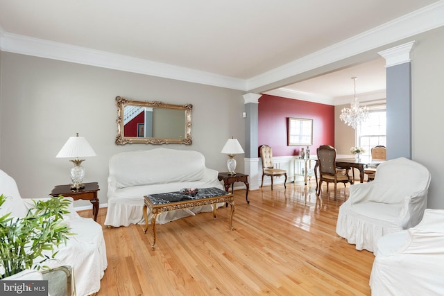 living room with crown molding, a notable chandelier, wood finished floors, and ornate columns