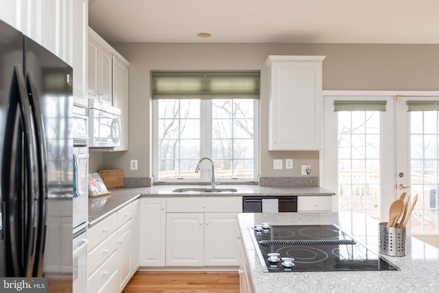 kitchen with black appliances, a sink, white cabinetry, and light stone countertops