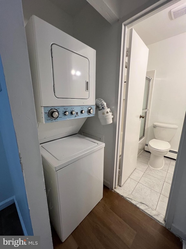 laundry area featuring hardwood / wood-style floors, stacked washer and clothes dryer, and a baseboard heating unit