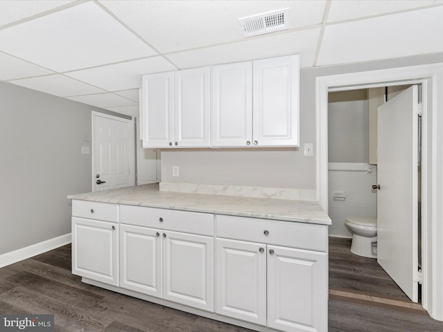 kitchen featuring white cabinetry, light stone counters, tile walls, dark hardwood / wood-style floors, and a drop ceiling