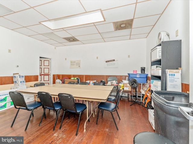 dining room with a drop ceiling, hardwood / wood-style floors, and wood walls