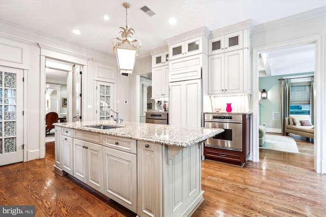 kitchen with sink, white cabinets, an island with sink, and stainless steel oven