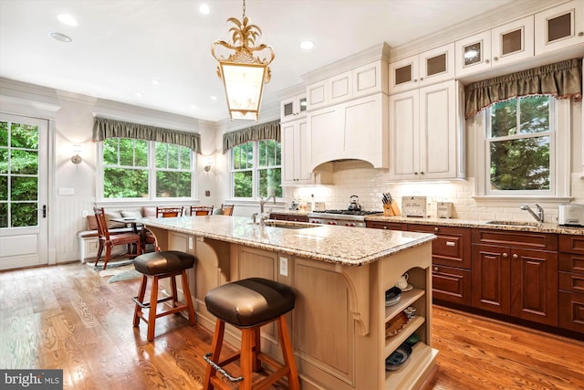 kitchen featuring sink, light hardwood / wood-style flooring, a breakfast bar area, an island with sink, and decorative light fixtures