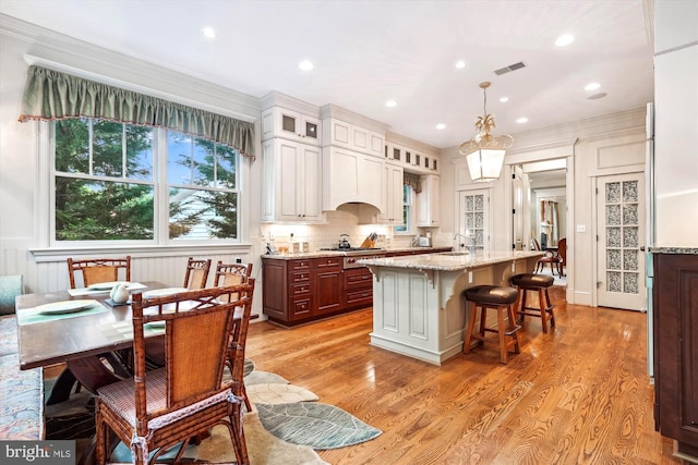 kitchen with a breakfast bar, stainless steel gas stovetop, hanging light fixtures, a kitchen island with sink, and light hardwood / wood-style flooring