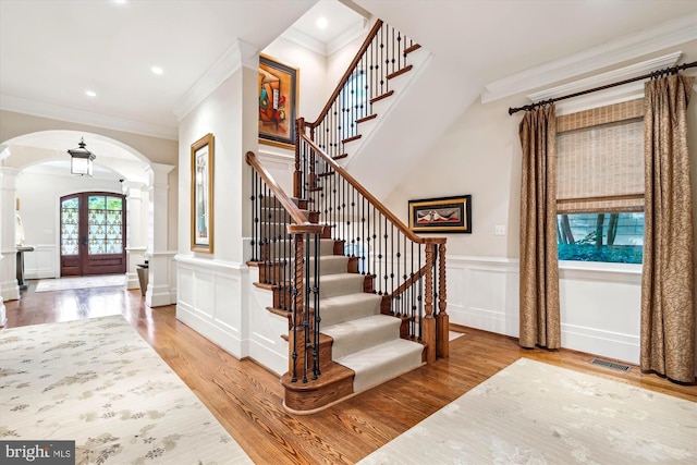 foyer entrance featuring hardwood / wood-style floors, ornamental molding, decorative columns, and french doors