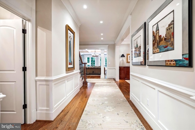 corridor with crown molding, wood-type flooring, and a chandelier