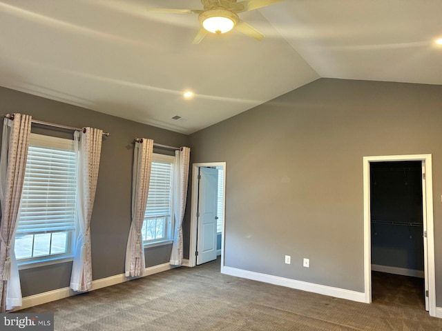 unfurnished bedroom with multiple windows, lofted ceiling, a spacious closet, and dark carpet