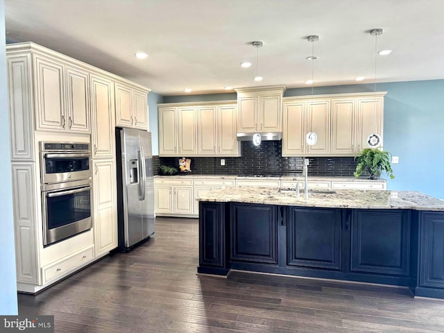 kitchen with appliances with stainless steel finishes, pendant lighting, sink, light stone counters, and a center island with sink