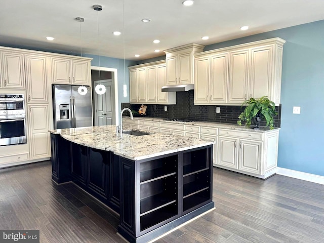 kitchen featuring sink, decorative light fixtures, appliances with stainless steel finishes, an island with sink, and light stone countertops