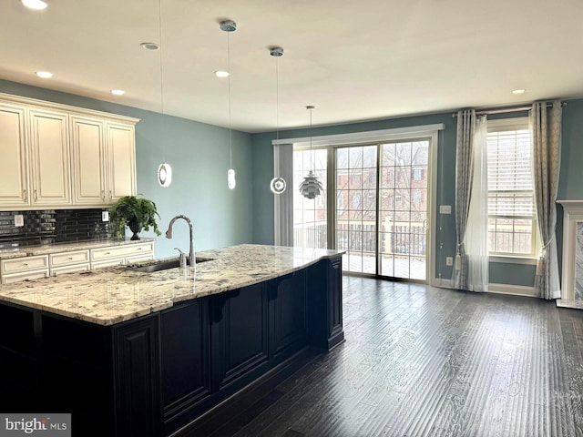 kitchen featuring sink, backsplash, light stone countertops, dark hardwood / wood-style flooring, and decorative light fixtures