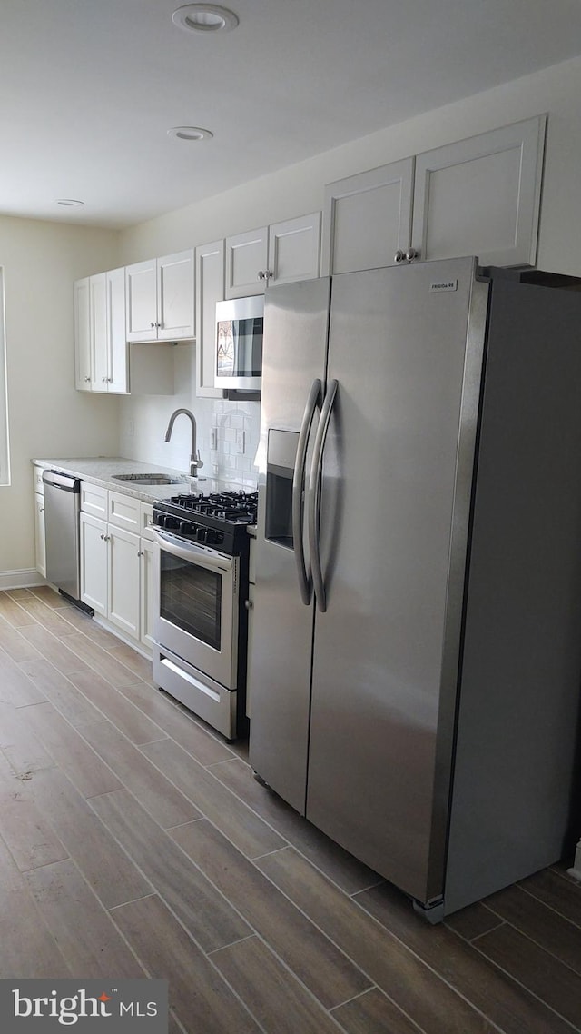 kitchen with appliances with stainless steel finishes, white cabinetry, sink, decorative backsplash, and hardwood / wood-style flooring