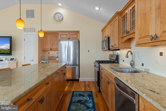 kitchen featuring vaulted ceiling, pendant lighting, sink, light stone counters, and stainless steel appliances