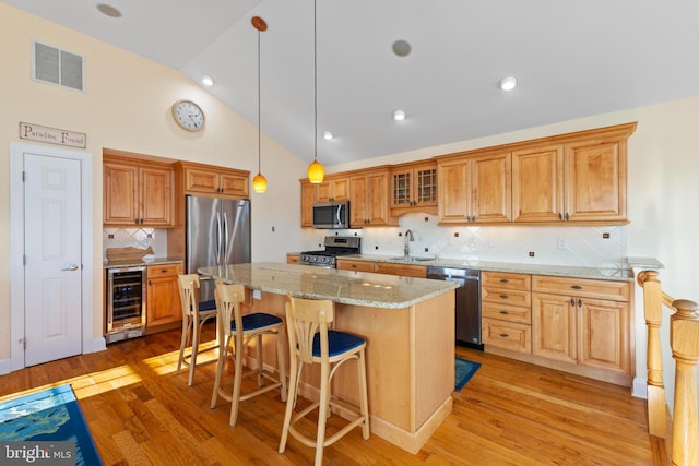 kitchen with pendant lighting, appliances with stainless steel finishes, a center island, wine cooler, and light stone counters