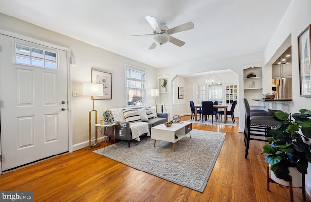 living room with built in shelves, wood-type flooring, and ceiling fan with notable chandelier