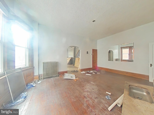 unfurnished living room with wood-type flooring, radiator, sink, and a textured ceiling