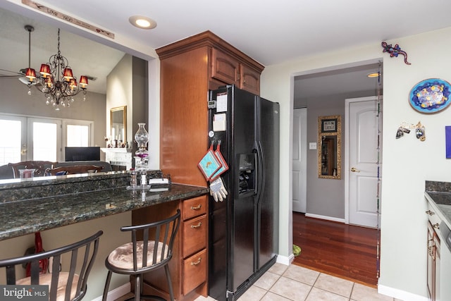 kitchen with black fridge, a notable chandelier, dark stone counters, and light tile patterned floors