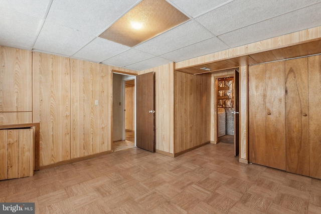 spare room featuring wooden walls, light parquet floors, and a drop ceiling