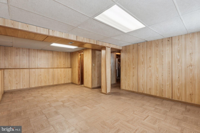 basement featuring light parquet flooring, a paneled ceiling, and wooden walls