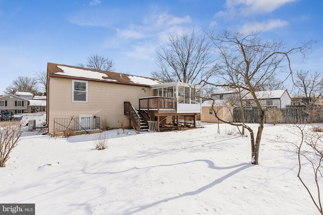 snow covered back of property with a wooden deck and a sunroom