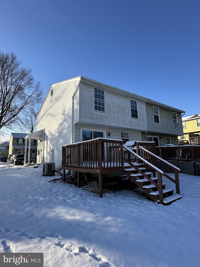 snow covered back of property with cooling unit and a deck