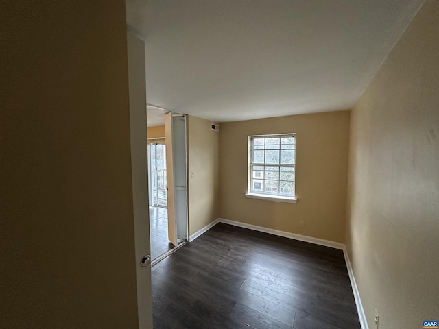 empty room with a wealth of natural light and dark hardwood / wood-style flooring