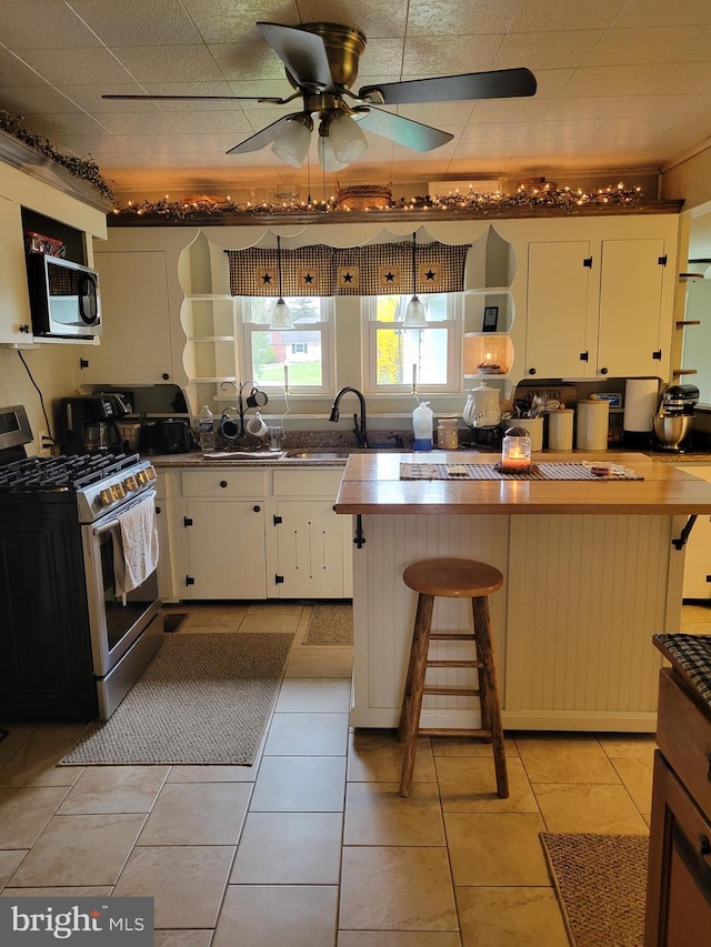 kitchen with light tile patterned floors, a breakfast bar, ceiling fan, appliances with stainless steel finishes, and white cabinets