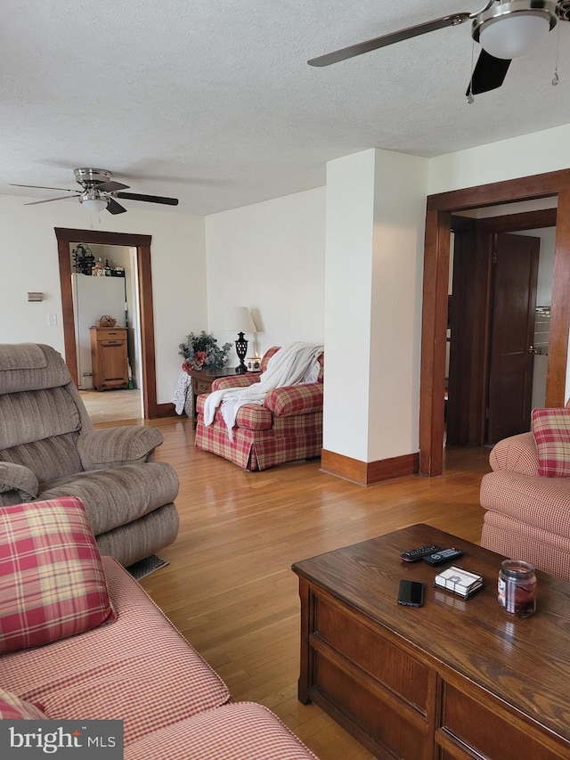 living room with a textured ceiling, ceiling fan, and light wood-type flooring