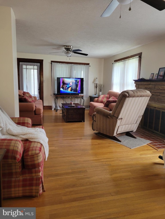 living room featuring ceiling fan, a textured ceiling, and light wood-type flooring