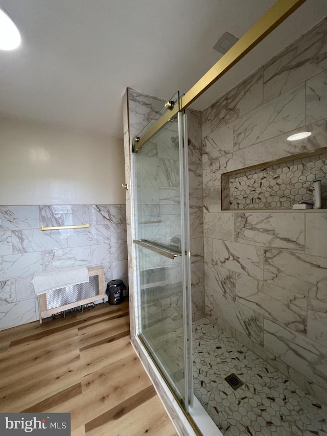 bathroom with hardwood / wood-style floors, an enclosed shower, and tile walls