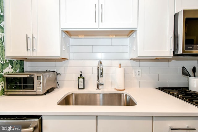 kitchen with white cabinetry, appliances with stainless steel finishes, sink, and backsplash