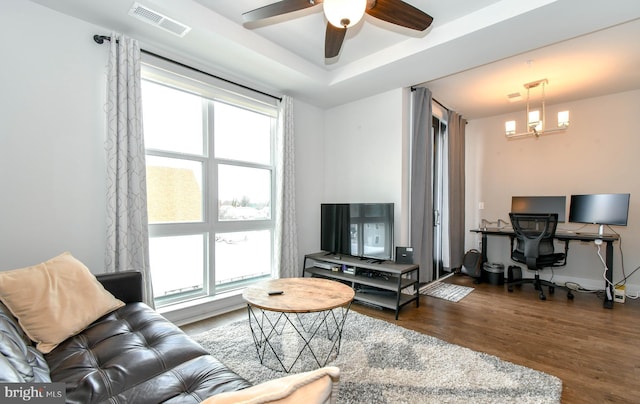 living room with a raised ceiling, dark hardwood / wood-style floors, and ceiling fan with notable chandelier