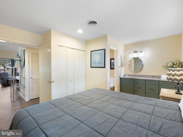 bedroom with wood-type flooring, connected bathroom, sink, and a textured ceiling