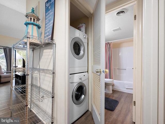 laundry room featuring dark wood-type flooring, stacked washer / dryer, and a textured ceiling