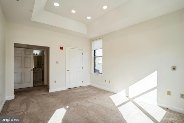 unfurnished bedroom with ensuite bathroom, a raised ceiling, and light carpet