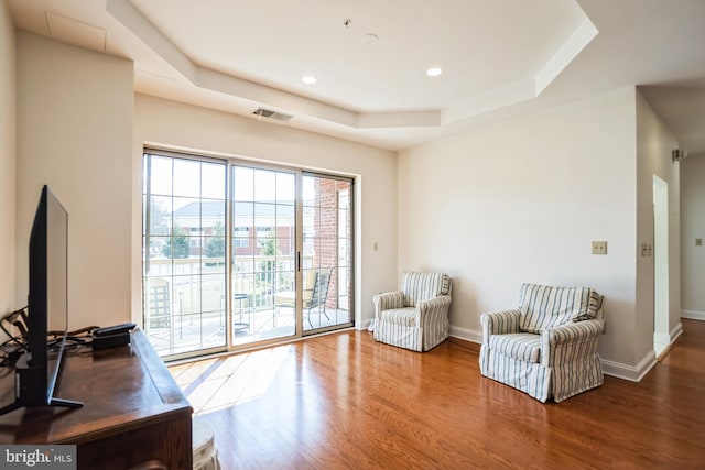 sitting room featuring wood-type flooring and a tray ceiling