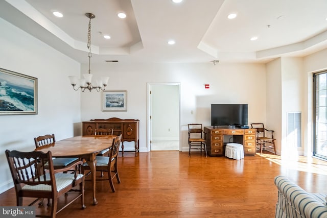 dining area featuring hardwood / wood-style flooring, a raised ceiling, and a notable chandelier