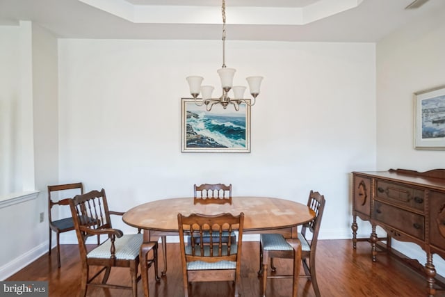 dining area featuring dark wood-type flooring, an inviting chandelier, and a tray ceiling