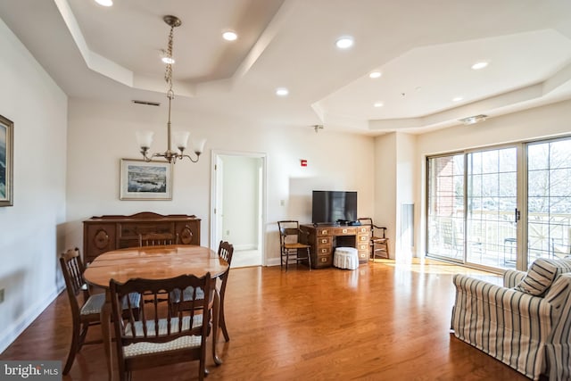 dining space featuring dark wood-type flooring, a raised ceiling, and a chandelier