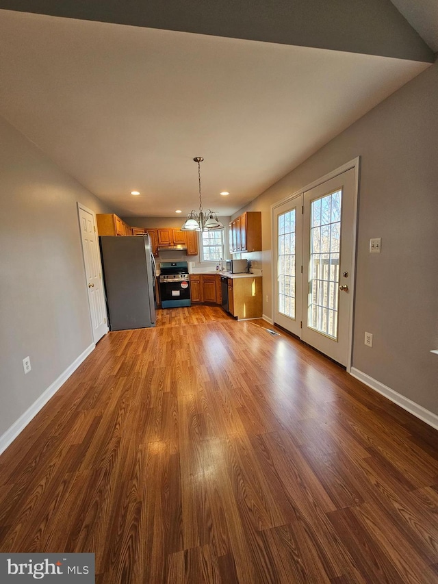 kitchen with appliances with stainless steel finishes, pendant lighting, hardwood / wood-style flooring, a notable chandelier, and kitchen peninsula