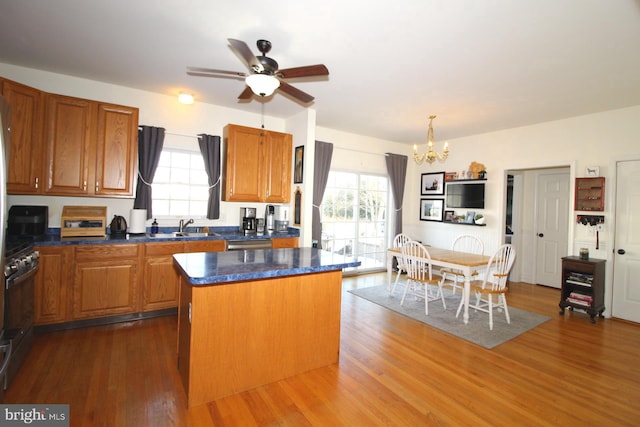 kitchen with dark wood-type flooring, sink, stainless steel gas stove, a kitchen island, and ceiling fan with notable chandelier